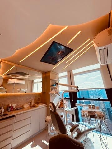 Sala clínica com cadeira odontológica, televisão no teto e vista panorâmica da cidade